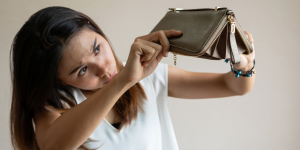 young woman looking at her empty wallet, which she has turned upside down