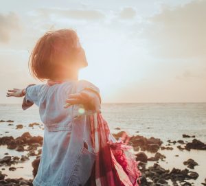 woman standing at a rocky shore, exalting in the light of the sunrise,