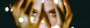 woman peering through her fingers with small white lights