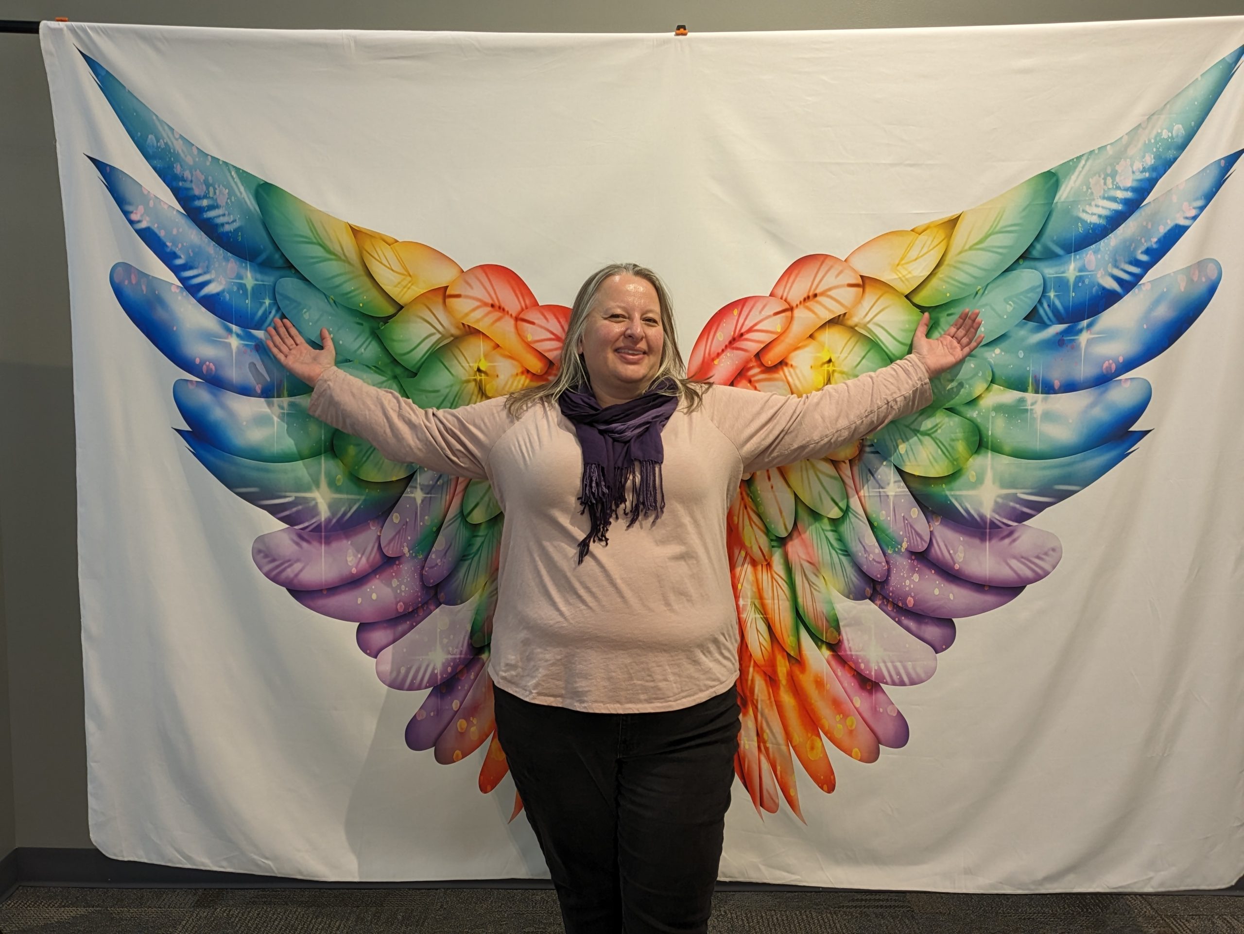 Christina posed in front of painted angel wings with arms extended