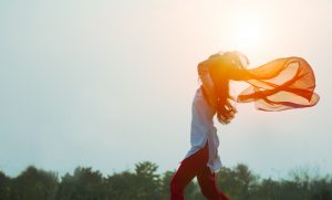 woman running across a field with scarf streaming behind her, silhouetted by the sun