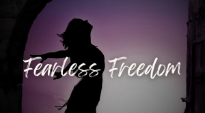 words Fearless Freedom in white over background of woman expressing freedom, standing with back arched and arms spread behind her, silhouetted in front of a purple sky