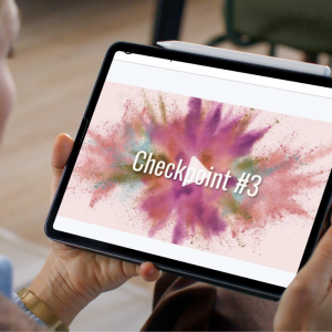 close-up of hands holding a tablet displaying the start of the Checkpoint #3 video