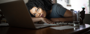 woman slumped onto desk, staring wearily at laptop screen